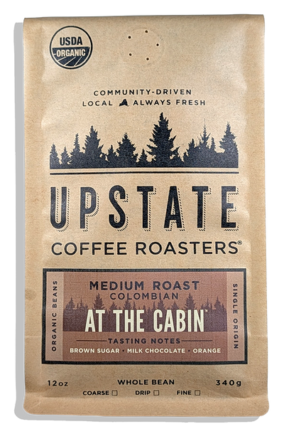 A 12 oz bag of Upstate Coffee Roasters 'At the Cabin' medium roast whole bean Colombian coffee, whole bean or ground, packaged in a kraft paper bag with black and brown text and graphics.