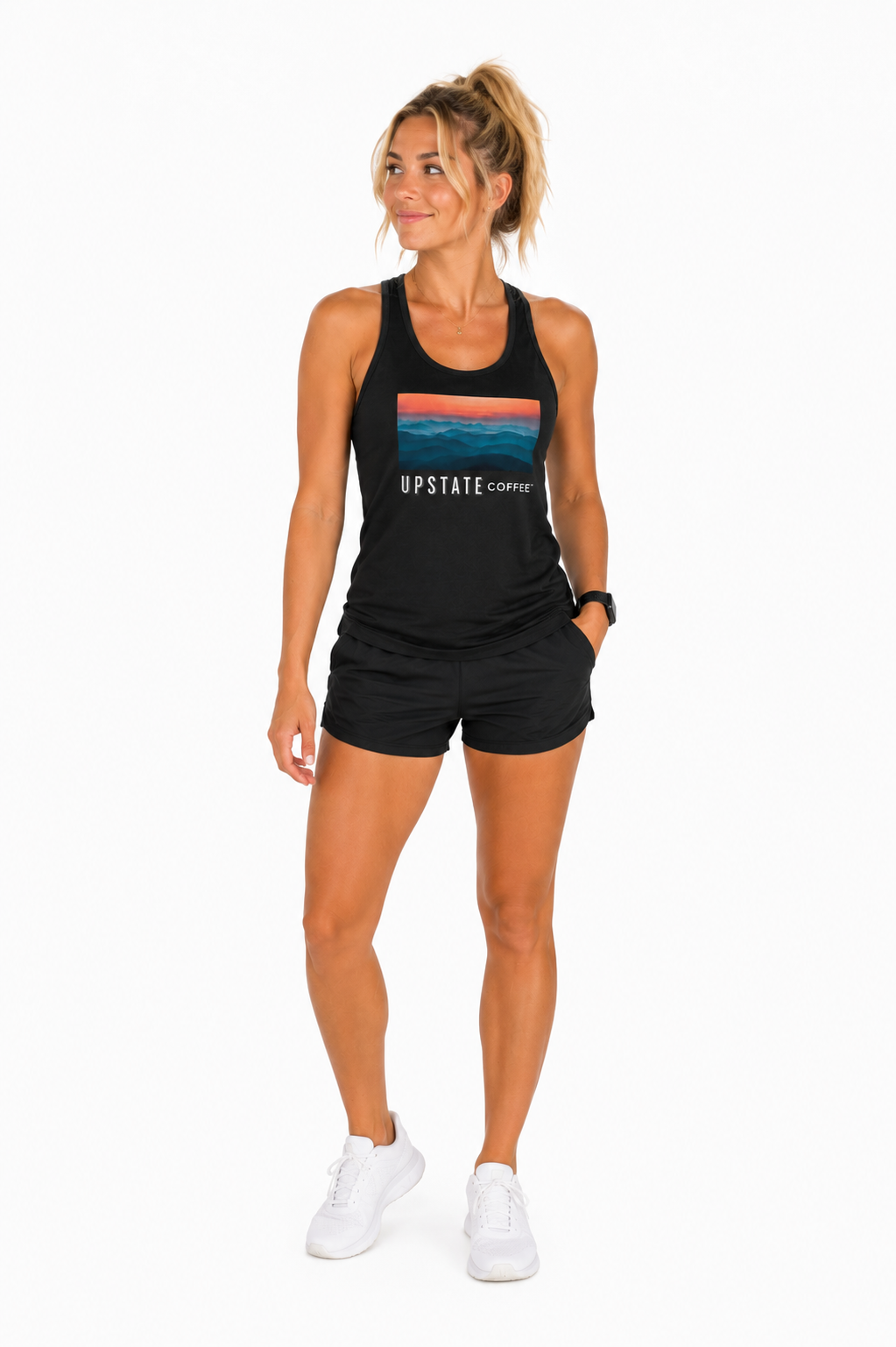 Woman model wearing a black tank top with an upstate coffee mountain scene graphic design and black shorts on a white backdrop