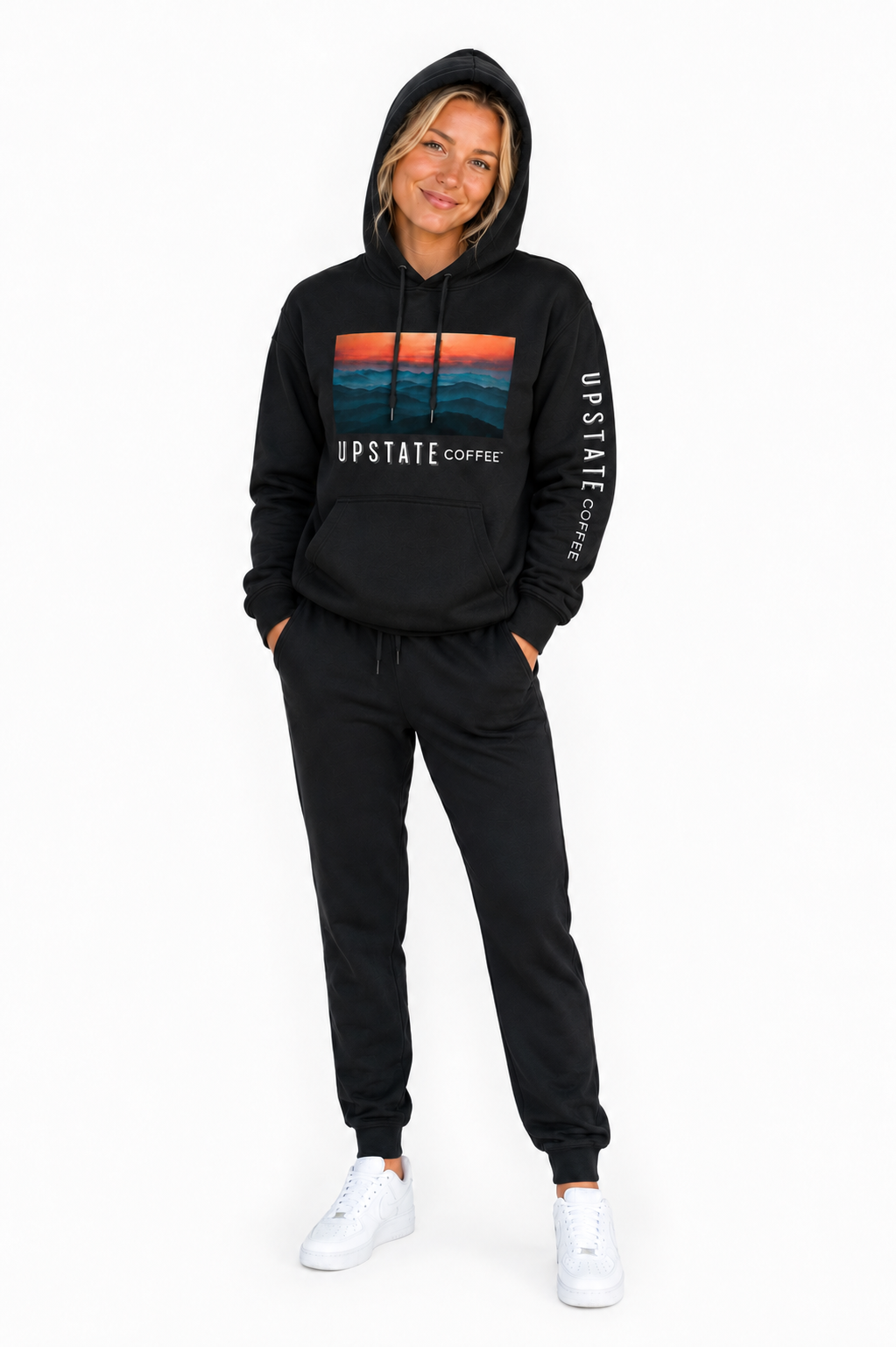 Blond Model wearing a black hoodie and jogger set with 'Upstate Coffee' mountain scene branding on a white background